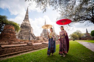 Two local Thai women walking past a temple holding parasols, a sight you might see when moving to Thailand