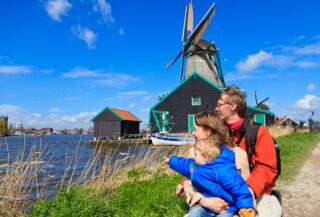 A family with a young child standing in front of a Dutch windmill on a clear sunny day