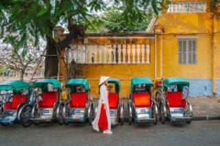 A Vietnamese woman walking past a row of parked rickshaws in Hoi An in Vietnam, one of the cheapest places to live in