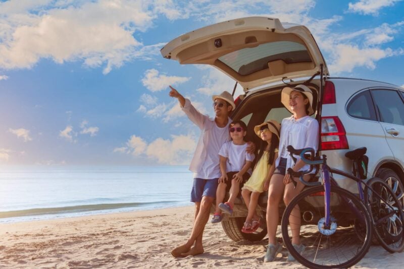 a happy family on holiday with their car, spending time at the beach knowing they are safe with international travel insurance coverage