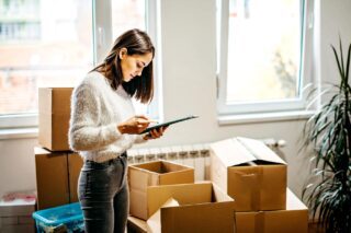 A woman standing in her home surrounded by cardboard boxes checking her moving abroad checklist