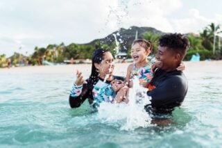 a happy mixed-raced expat couple playing with their daughter in the sea