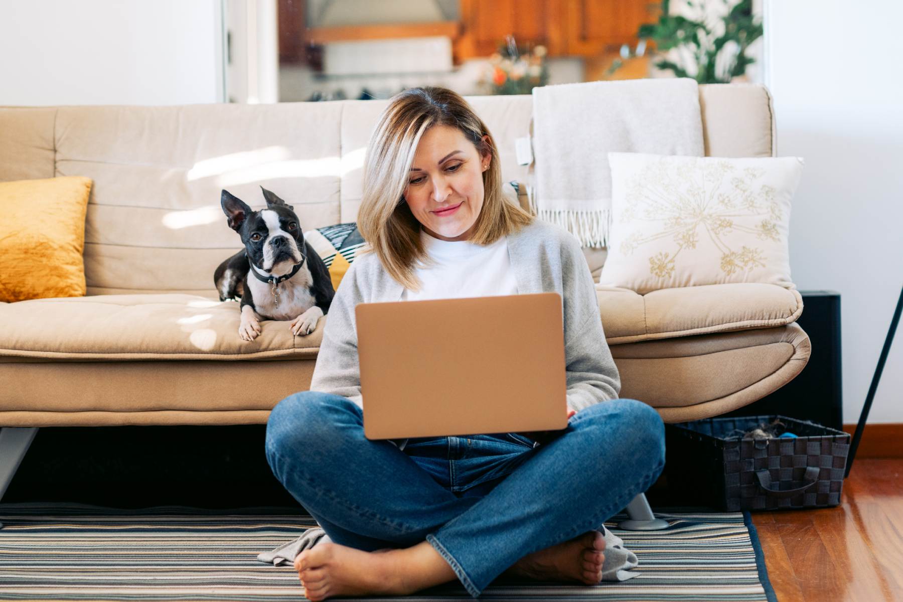 a female expat working remotely from home on her laptop with her dog sitting on the couch behind her