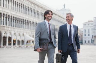 Two smiling businessmen walking across St. Mark's Square in Venice, having secured an Italy work visa