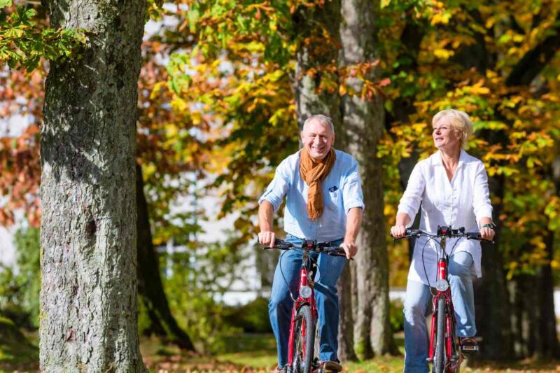 A happy senior couple cycling on bicycles through a leafy park after retiring in Germany