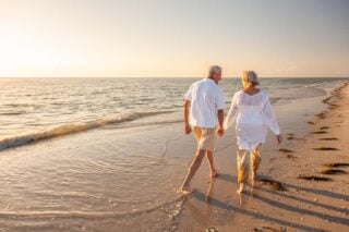 a happy couple retiring abroad, enjoying a stroll along a beach at sunset