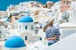 a happy couple looking across the rooftops of Santorini island, after moving to Greece