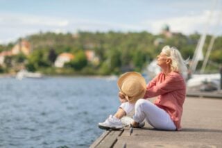 Senior woman sitting peacefully on the edge of a dock, gazing out to sea, feeling grateful for her decision to retire in Sweden.