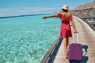 a woman traveling abroad, walking along a boardwalk in the Maldives pulling her suitcase behind her