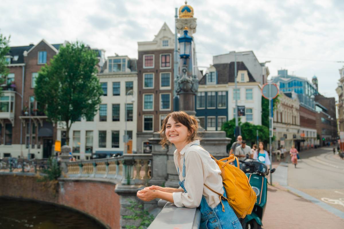 a happy female traveler standing on a bridge over a canal in Amsterdam, Netherlands, one of the best destinations for solo travel for women