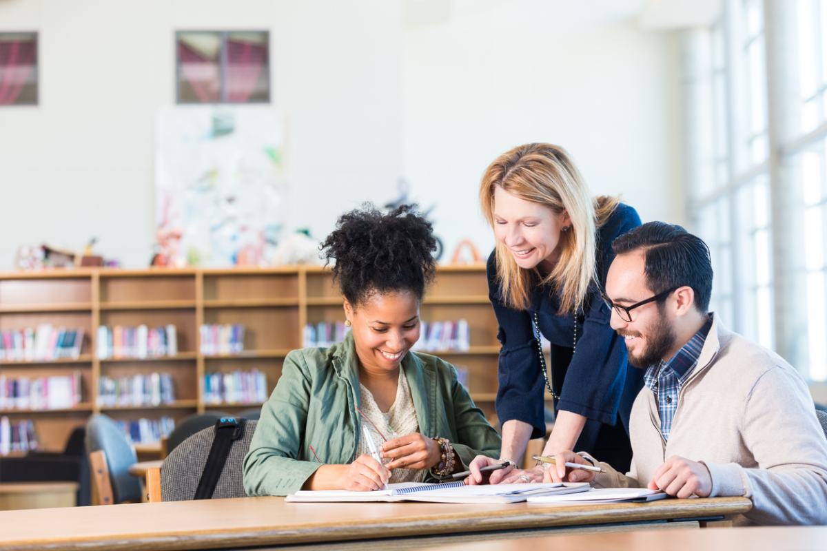 A diverse group of adults studying abroad in a large college library, learning a foreign language