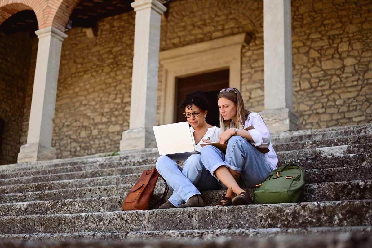 two university students sitting on stairs outside a building on campus in Italy