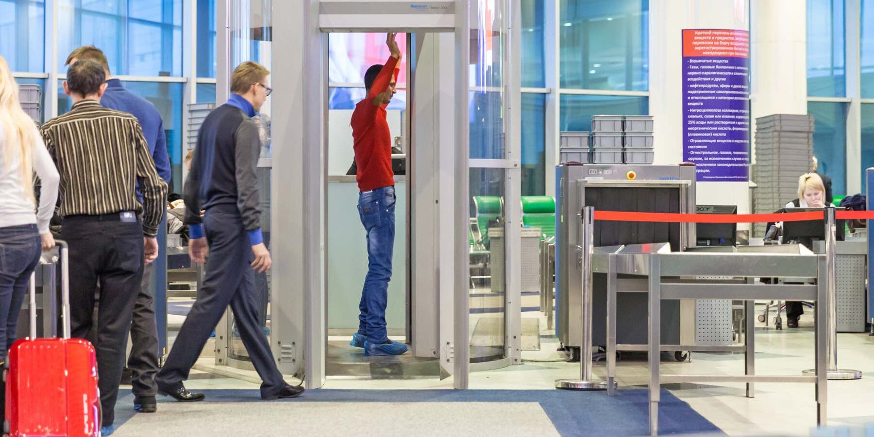 a male passenger standing in a full-body scanner at airport security, having booked a window seat on a plane