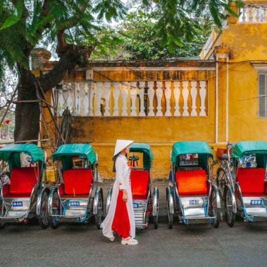 A Vietnamese woman walking past a row of parked rickshaws in Hoi An in Vietnam, one of the cheapest places to live in