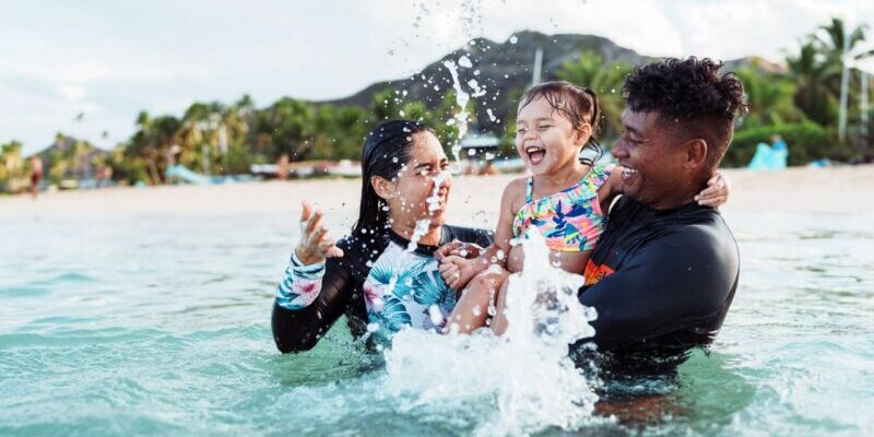 a happy mixed-raced expat couple playing with their daughter in the sea