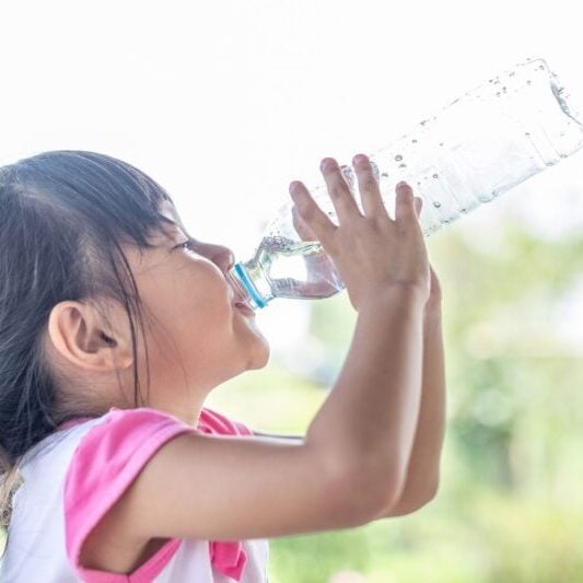 a little girl drinking water from a bottle after learning some healthy travel tips