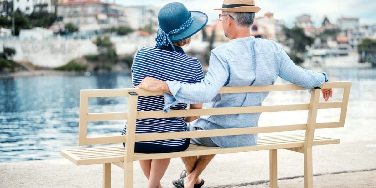 a retired couple sitting on a bench overlooking the sea after moving to Greece and seeking expat financial advice