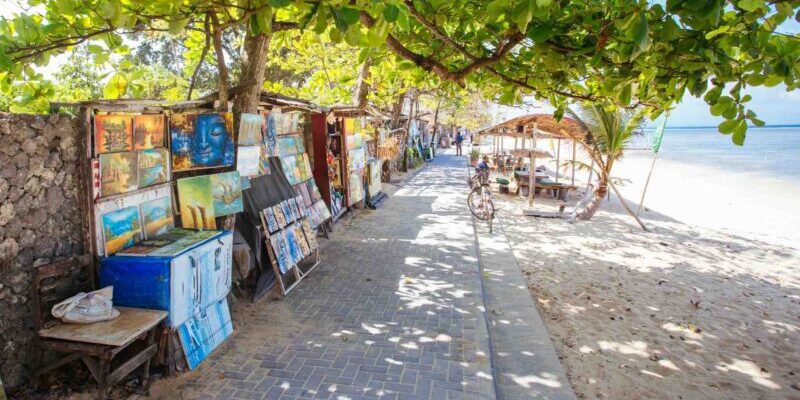 a selection of colorful paintings lined up along a beach in Sanur, Bali