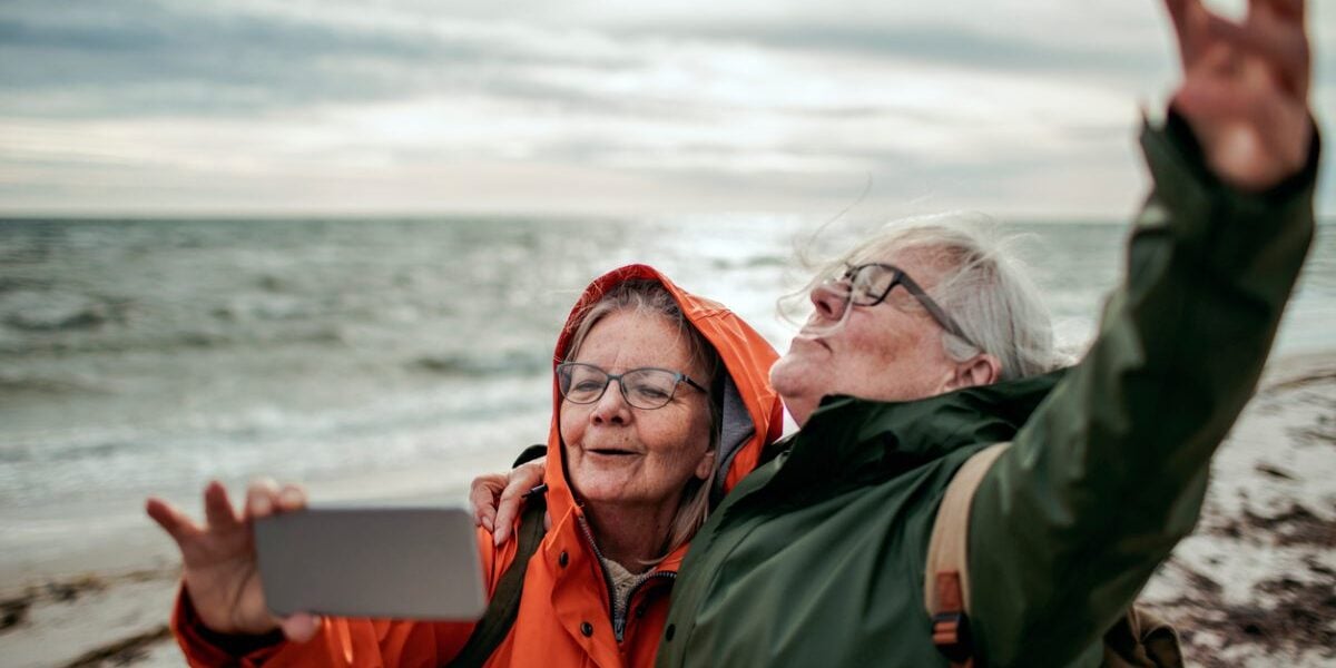 Two happy senior women taking a selfie by the sea, enjoying the benefit of fresh air which you get when you retire in Sweden