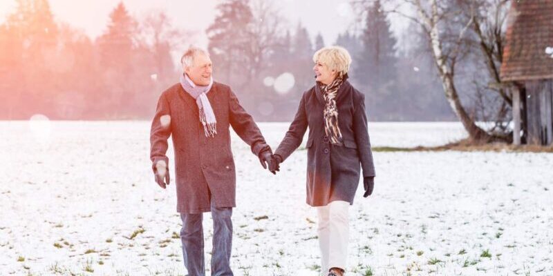 A senior couple walking hand in hand across a snowy field in Germany