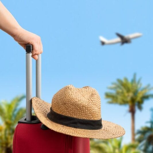 someone pulling their suitcase and getting ready for a holiday, with tips for traveling abroad in mind, as a plane takes off in the background