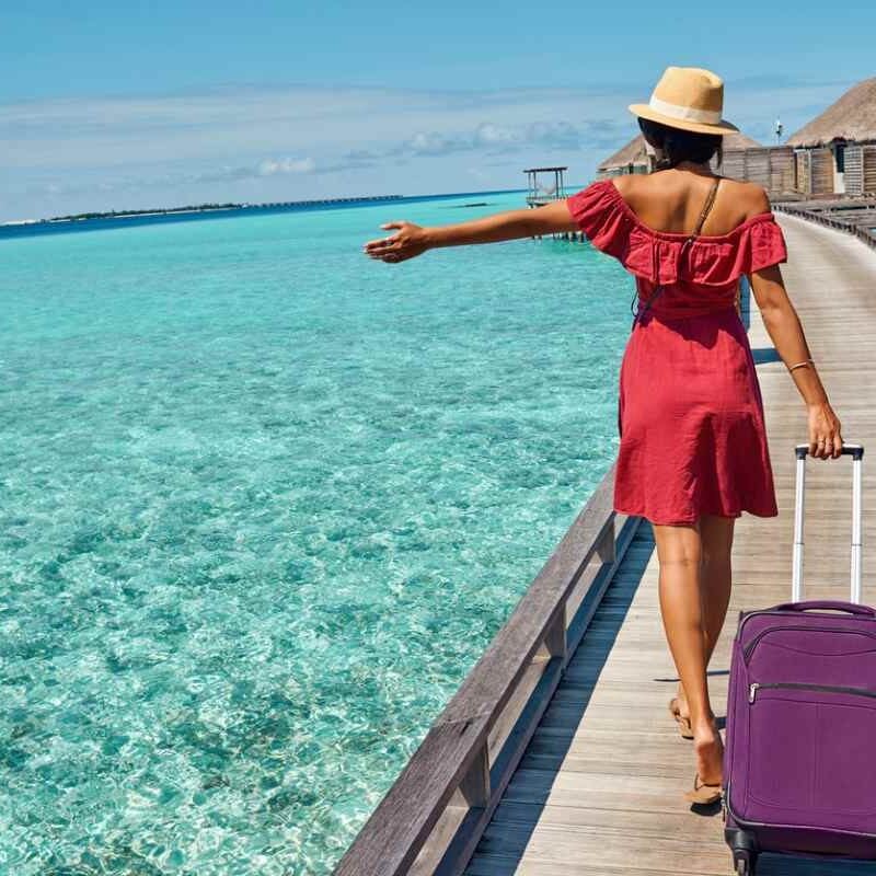 a woman traveling abroad, walking along a boardwalk in the Maldives pulling her suitcase behind her