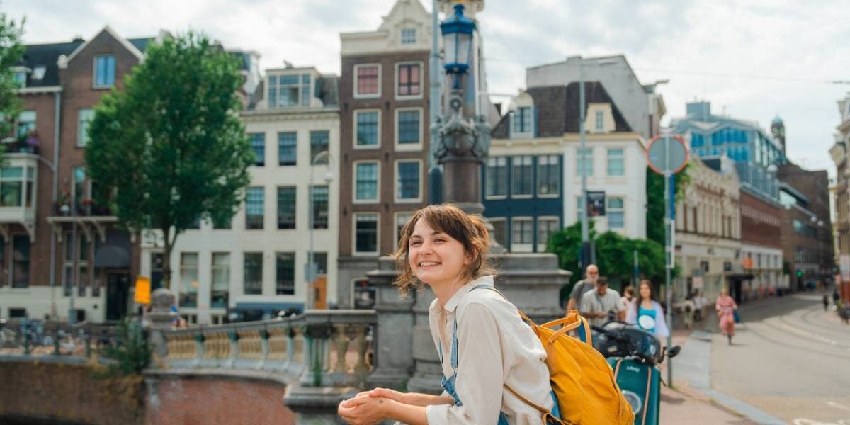 a happy female traveler standing on a bridge over a canal in Amsterdam, Netherlands, one of the best destinations for solo travel for women